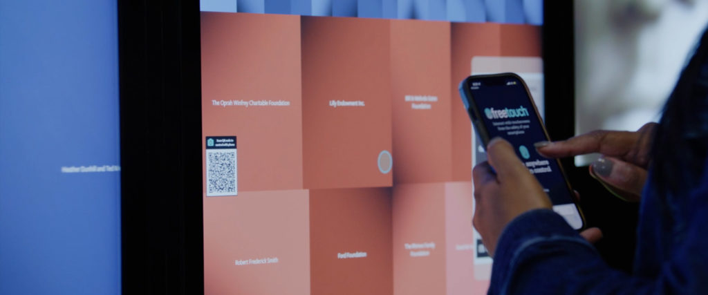 A user uses their smartphone to touchless interact with the interactive donor wall.